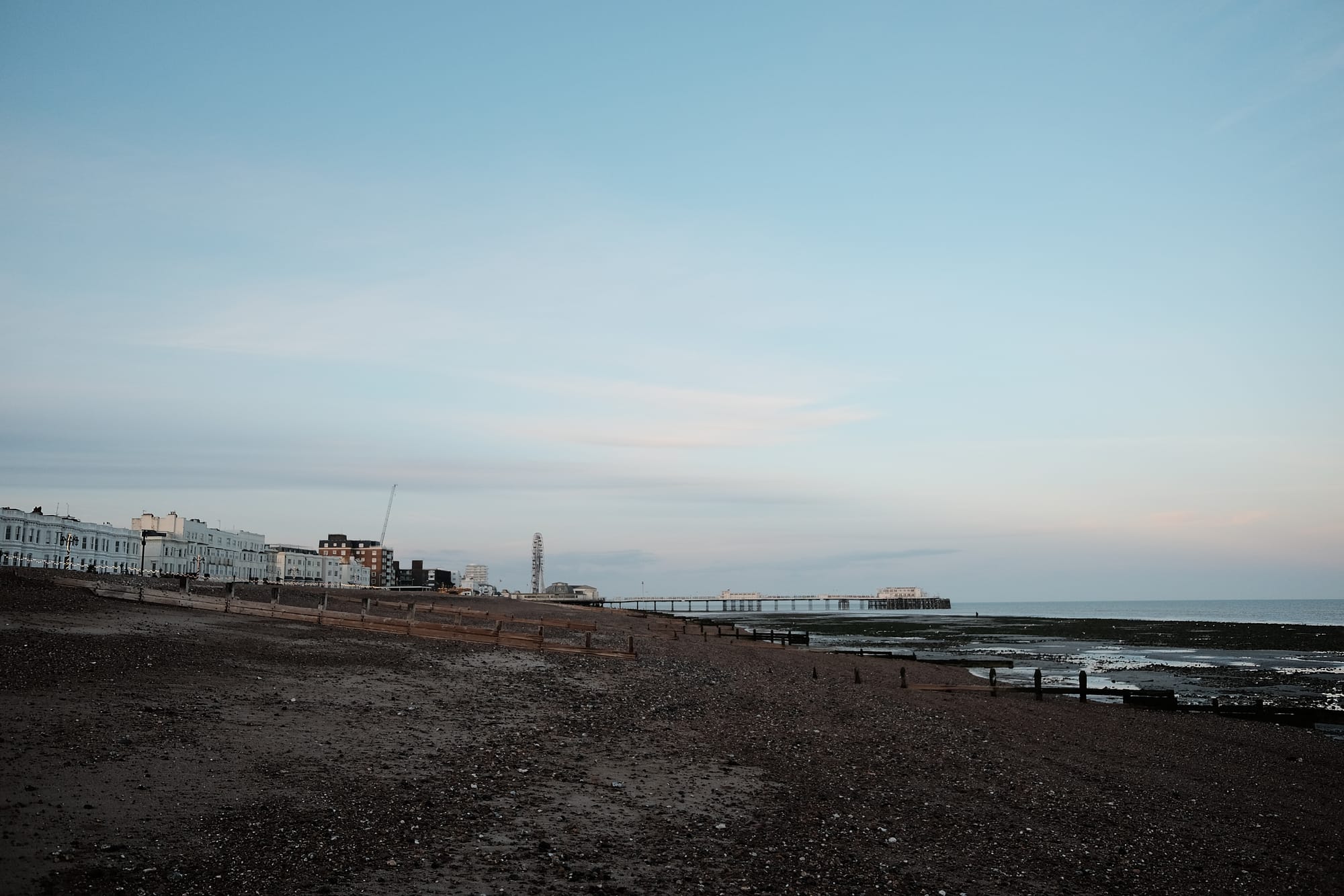 Worthing beach at low tide: sand and shingle slopes down to the sea with a pier in the distance and a Ferris wheel beyond it.