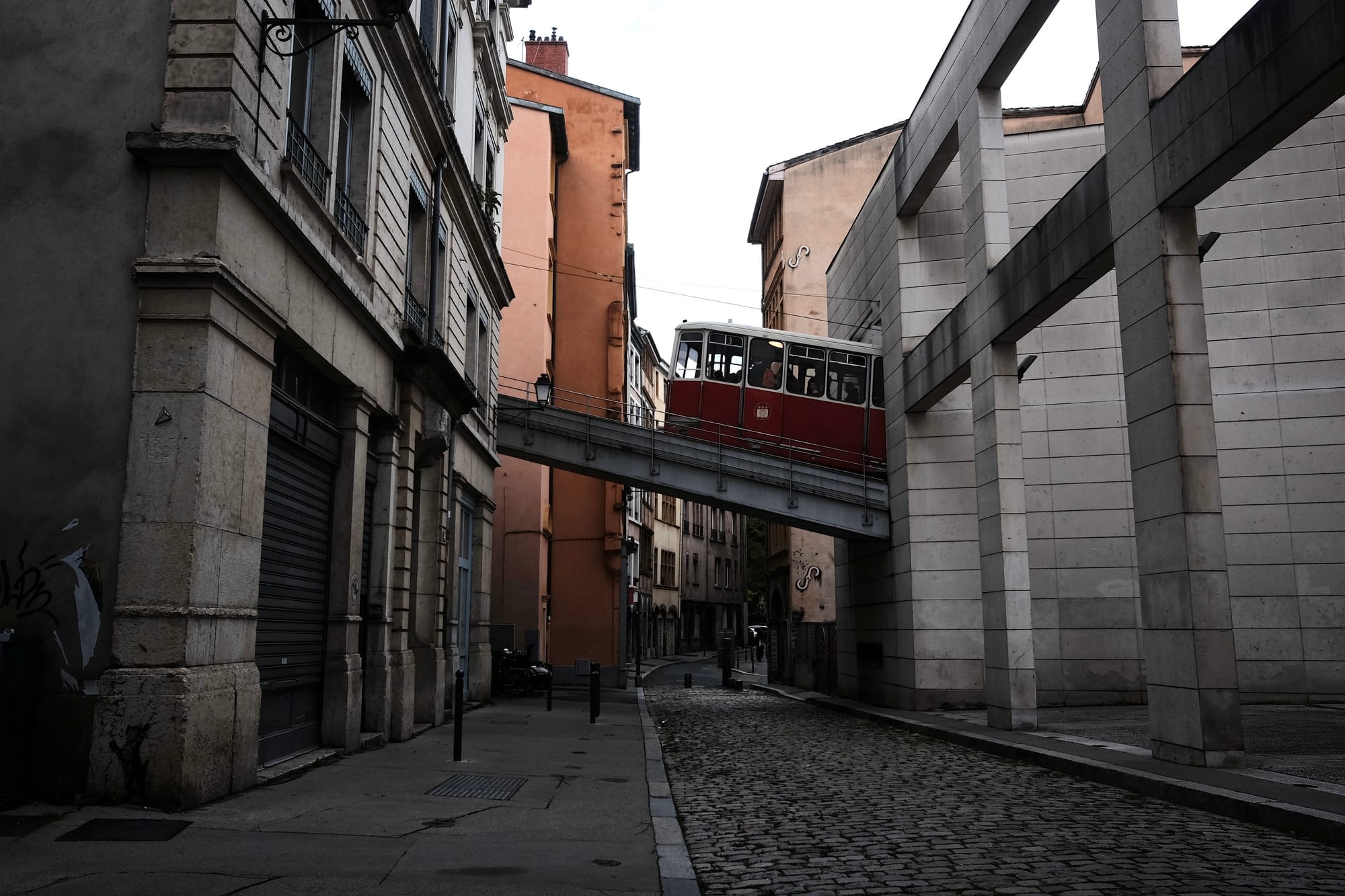 A red and white funicular carriage crosses an inclined bridge over a narrow streetin Lyon.