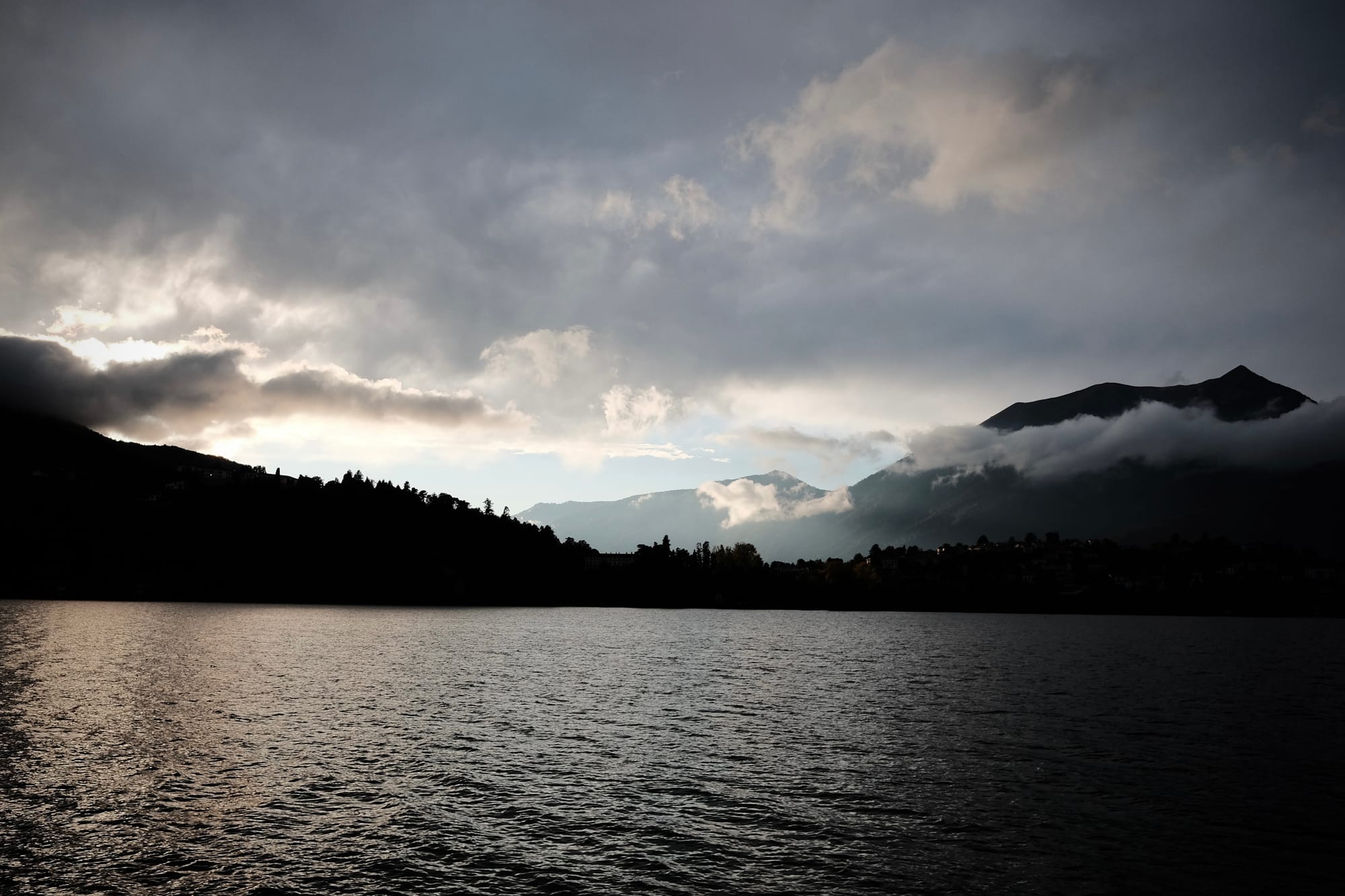 Evening light over Lake Como, with distant mountains silhouetted against a cloudy sky.