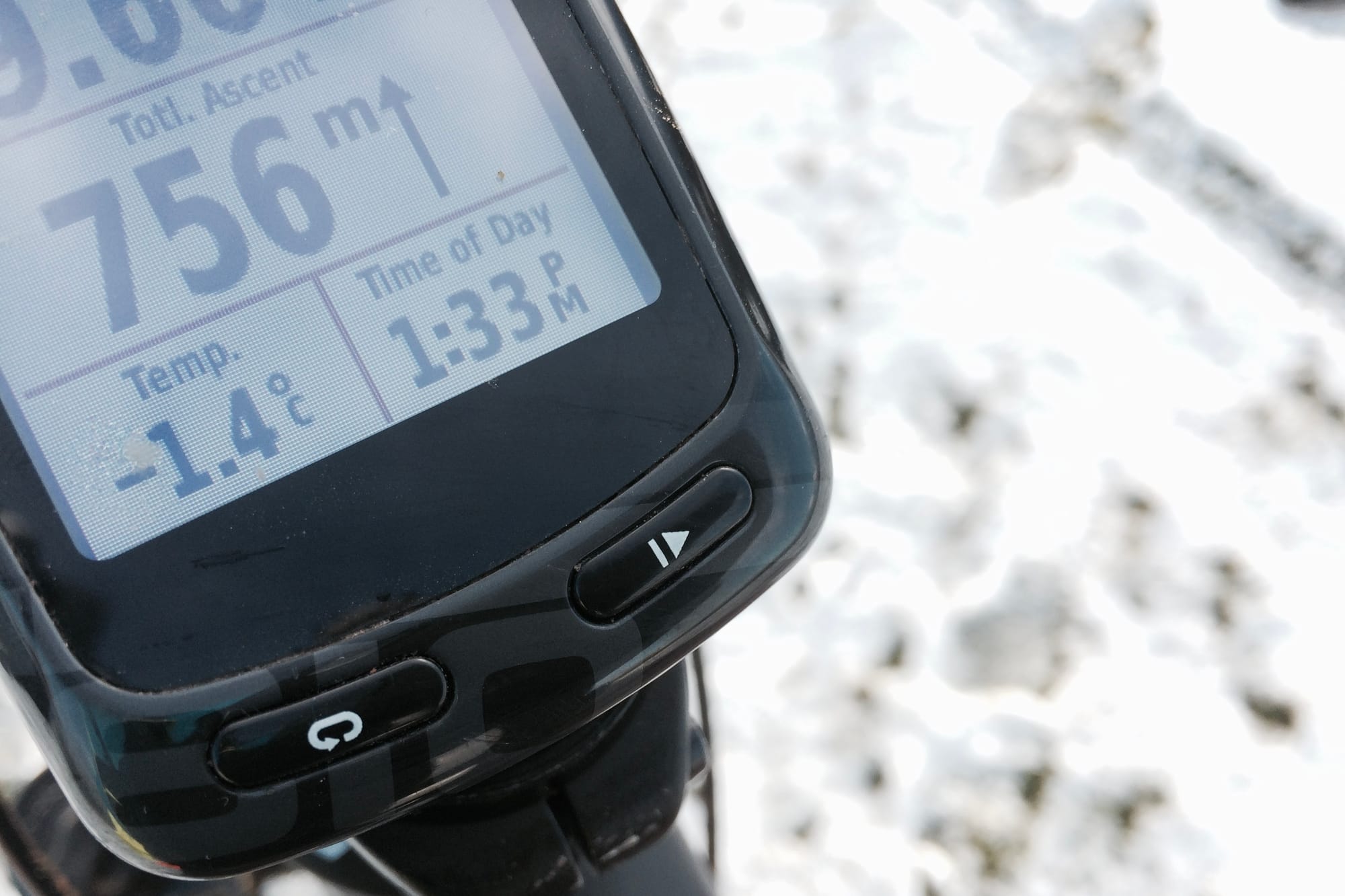 A GPS bike computer against a snowy background displays 756m ascent, temperature -1.4C and time of day 1.33pm.