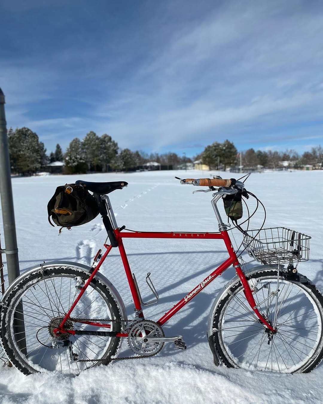 A red bike with a saddle bag and basket stands in deep snow.