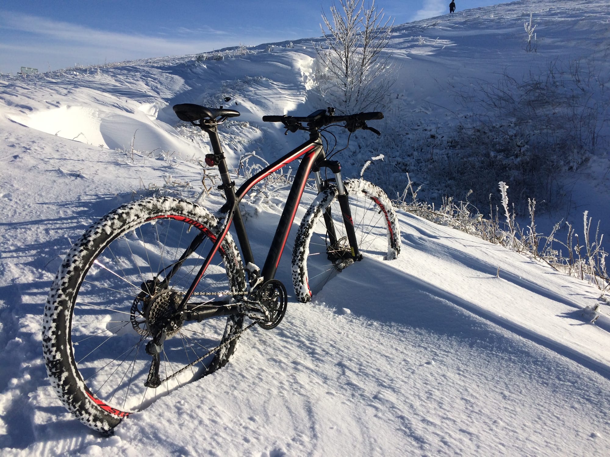 A black and red mountain bike stands in deep snow on the top of a hill.