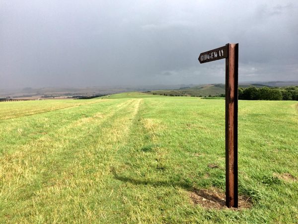 A rusty signpost points along the Ridgeway National Trail, rolling green hills in the background.