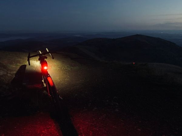 A bike leans on the bench at the top of the hill, its red rear and white front lights bright in the darkness.