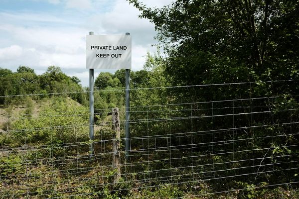 Behind a barbed wire fence, a sign amongst the trees reads: "Private land."