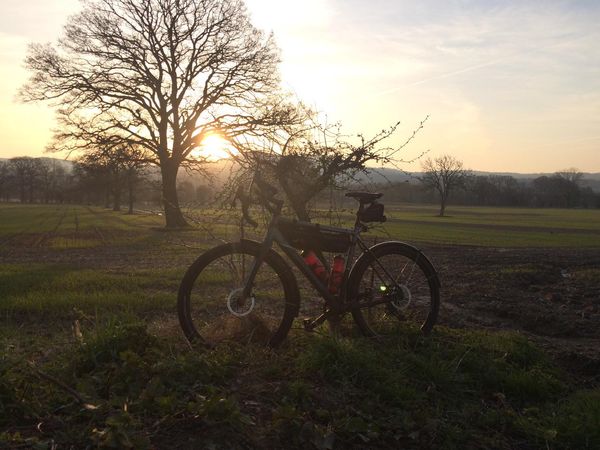 A gravel bike silhouetted against trees and hills at sunrise.
