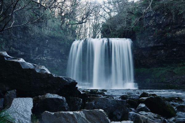A waterfall called Sgwd-yr-Eira, The Falling of the Snow, makes a white curtain as it plunges into a pool below.