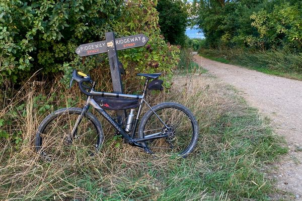 A bike leans on a signpost pointing to the Ridgeway byway in either direction, another track to the right.