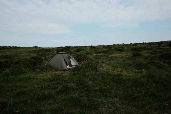 A small child, just visible, sleeps in a green tent against the green backdrop of Dartmoor.